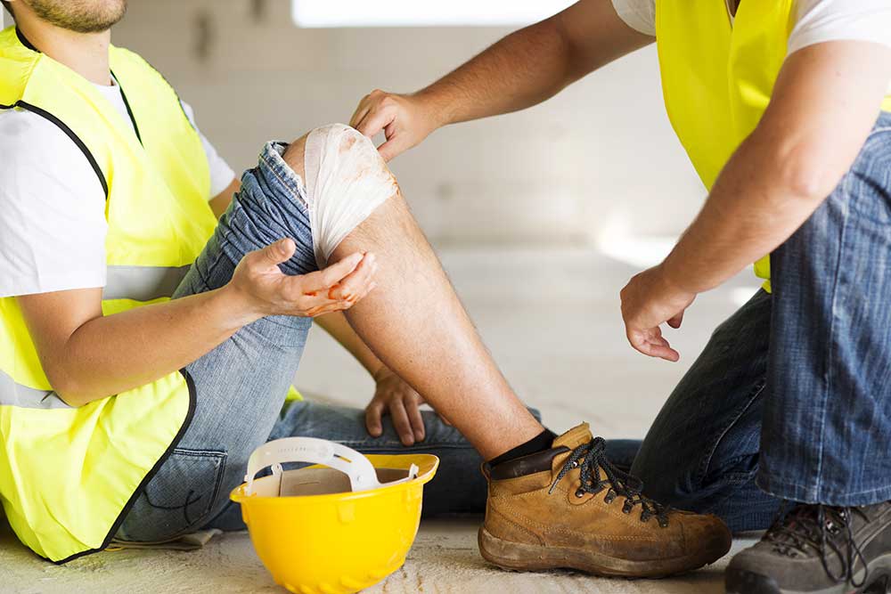 Worker receiving first aid for a knee injury at a construction site.