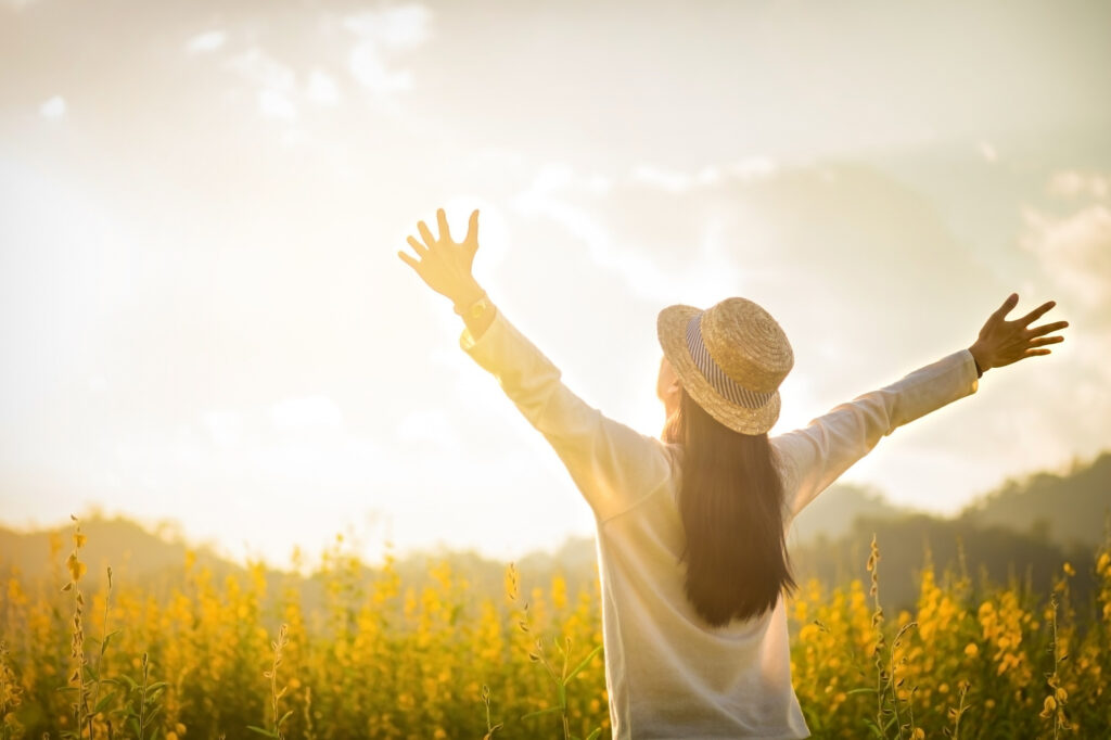 A person in a hat joyfully raises arms in a sunlit field.